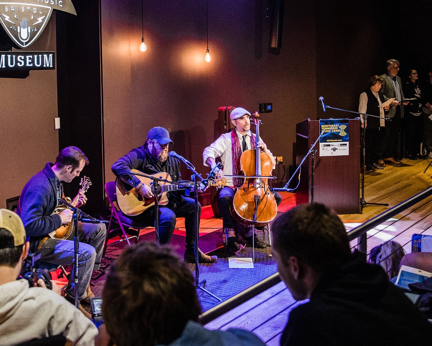 Musicians playing guitar, mandolin, and cello for a packed room at the Birthplace of Country Music Museum